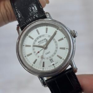 A hand holds a silver Epos wristwatch with a white multi-dial face, bold hour markers, and a black leather strap, showcasing its classic design.