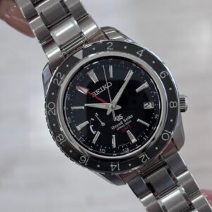 Close-up of a hand holding a polished stainless-steel Seiko wristwatch with a black dial, rotating bezel, date window, and silver bracelet, conveying precision and craftsmanship.