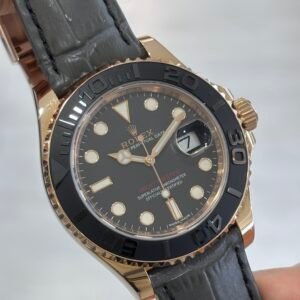 A close-up of a hand holding a Rolex Yacht-Master watch with a black dial, gold case, black bezel, and black leather strap.
