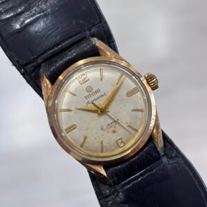 A vintage gold-tone Titoni wristwatch with a worn silver dial, gold hands and markers, and a cracked black leather strap, photographed against a pale background.