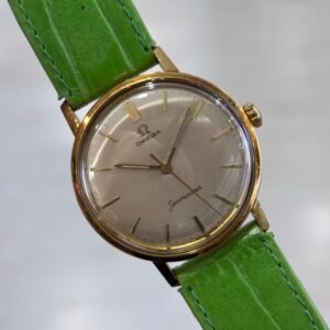 A vintage gold-tone Omega Seamaster wristwatch with a silver dial and bright green leather strap, photographed against a soft gray background.