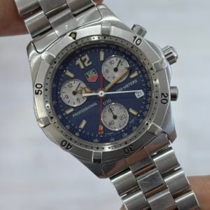 A hand holds a stainless-steel TAG Heuer chronograph watch with a blue dial, three silver subdials, date window, and marked bezel; precise, rugged design.